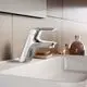 Ein verchromter Wasserhahn von Ideal Standard, montiert an einem weißen Waschbecken, mit einer schlichten, modernen Form und einer Seifenablage im Hintergrund.
